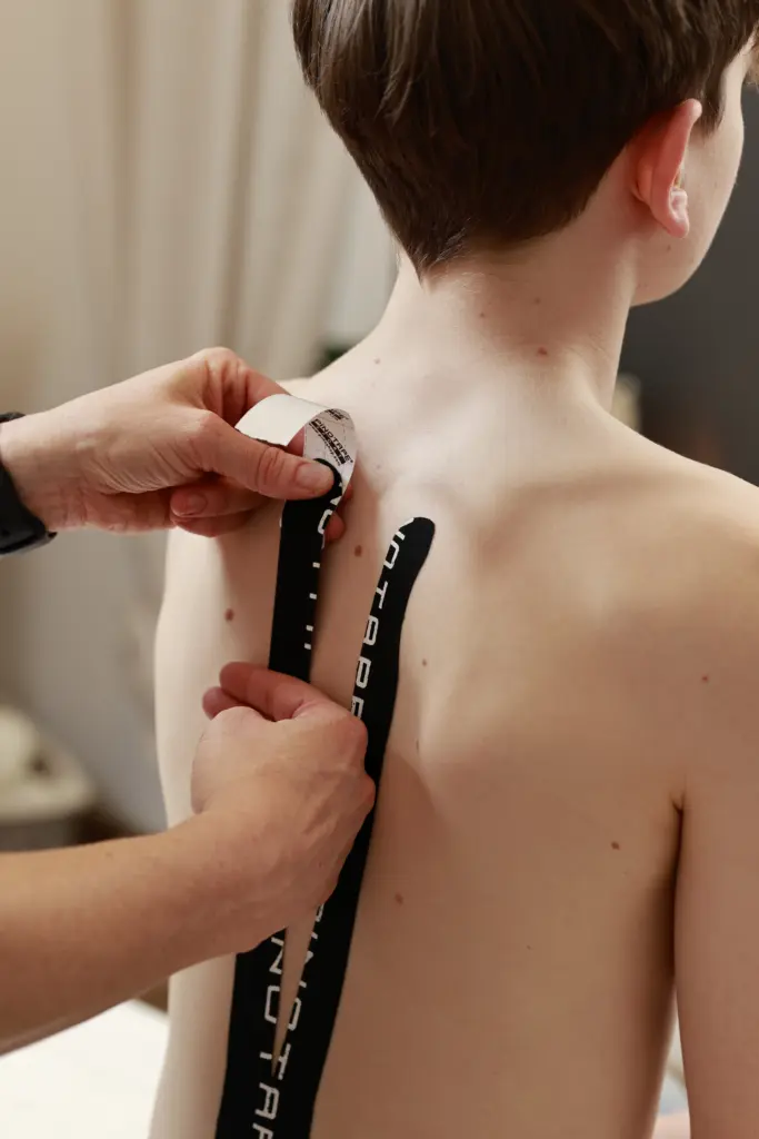 Physiotherapeutin klebt elastisches Kinesio-Tape auf den Rücken eines Patienten zur Schmerzlinderung
