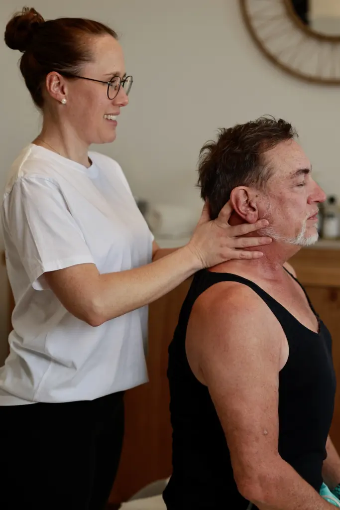 Physiotherapeutin massiert den Schulter- und Nackenbereich einer sitzenden Patientin zur Lösung von Verspannungen